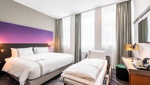 Une chambre d’hôtel avec deux lits, un bureau, une chaise, une télévision et une grande fenêtre avec des rideaux.