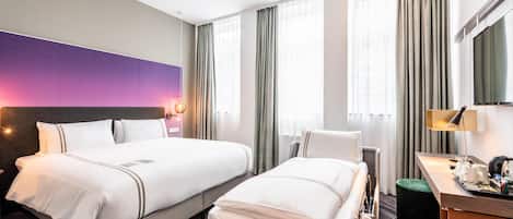 A hotel room with two beds, a desk, a chair, a TV, and a large window with curtains.