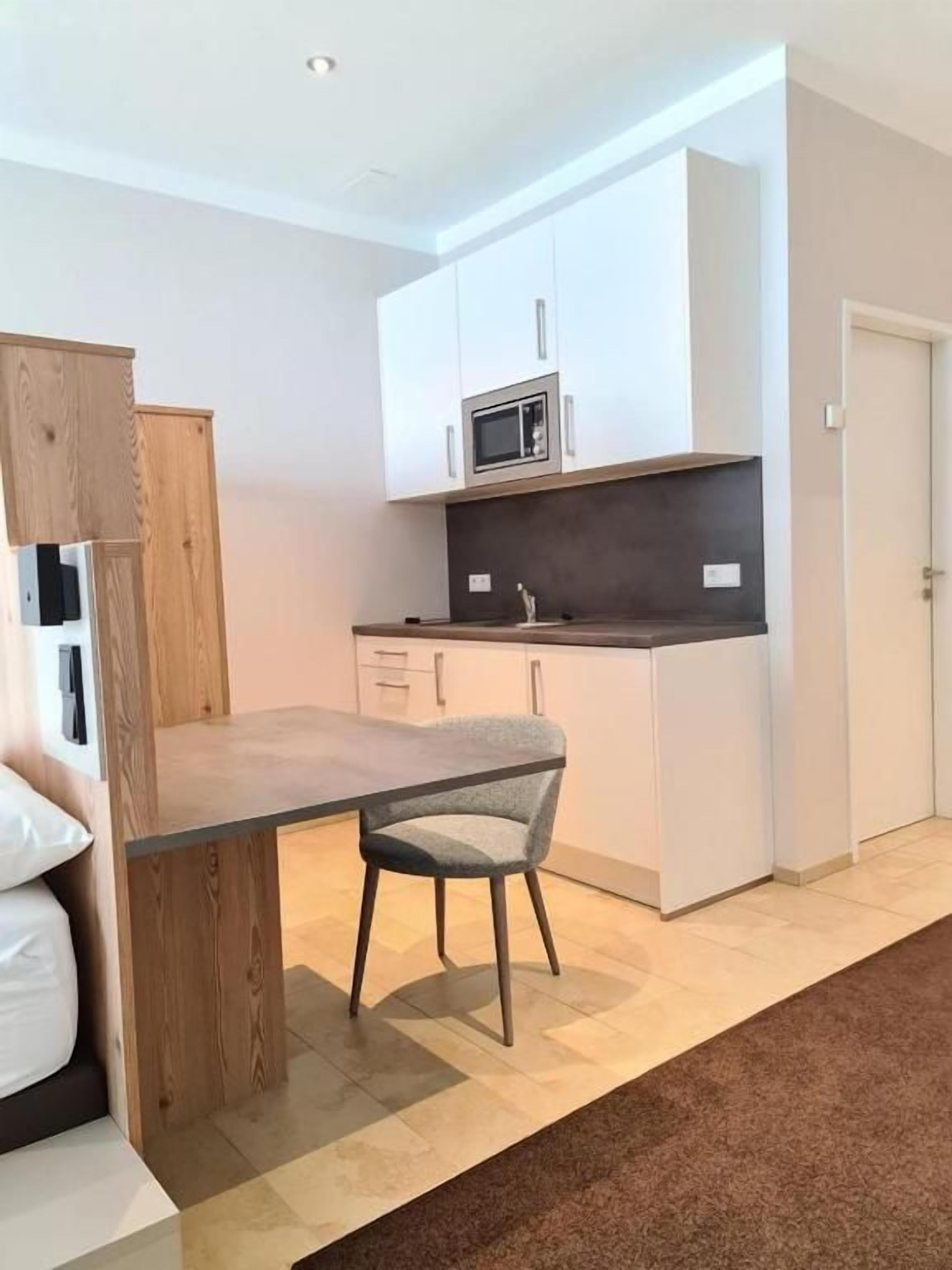 A compact kitchen with white cabinetry, a microwave, and a dining area with a table and chair.