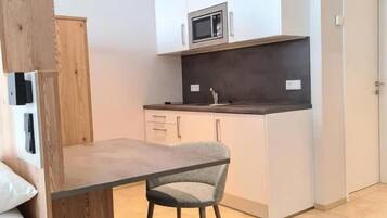 A compact kitchen with white cabinetry, a microwave, and a dining area with a table and chair.