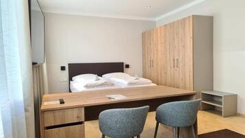 A modern bedroom with a wooden bed, a desk, two chairs, and a wardrobe.