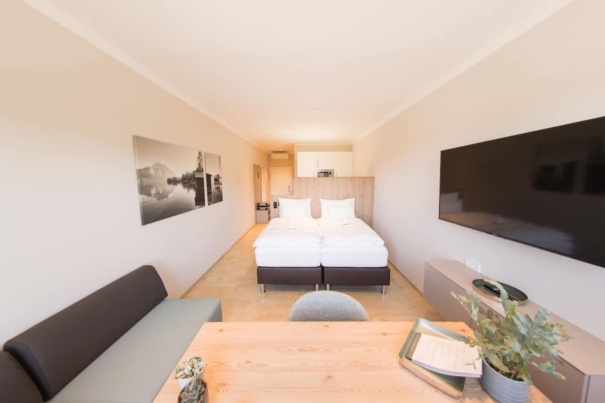 A modern hotel room with a bed, a TV, a desk, and a couch.