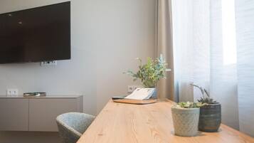 A modern room with a flat-screen TV mounted on the wall, a wooden table with a potted plant, a chair, and a small cabinet with a tray.