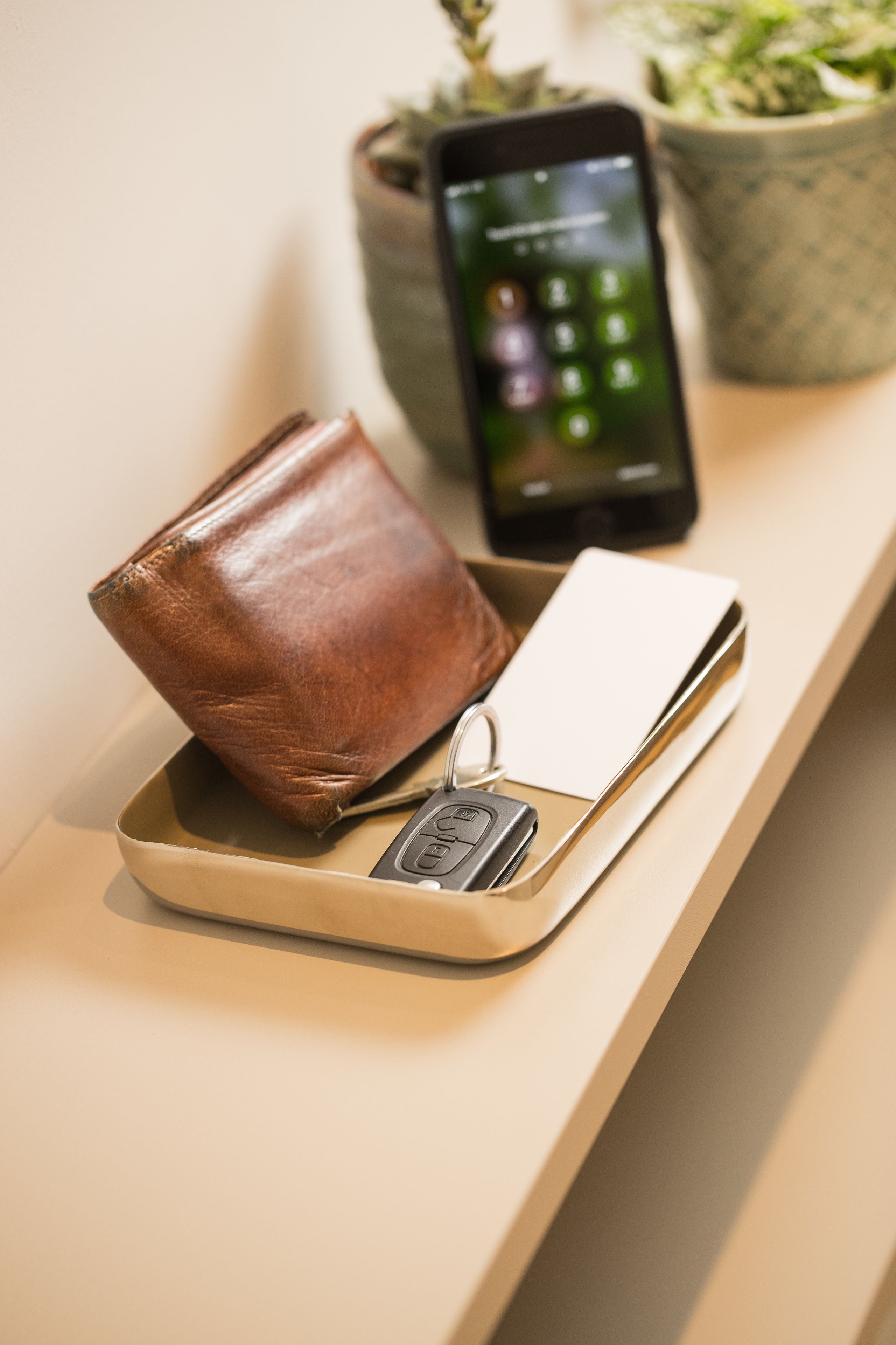 Una cartera, llaves y un teléfono inteligente sobre una bandeja.