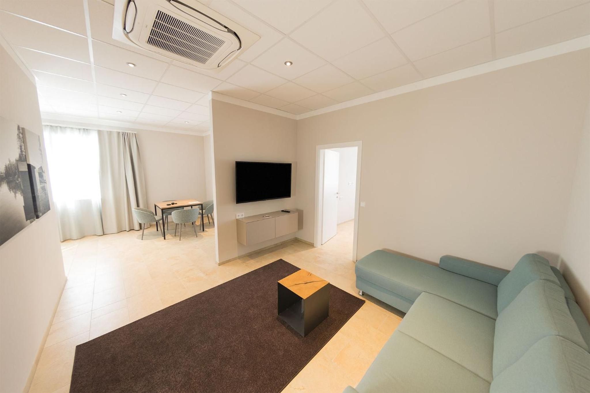 Ein modernes Wohnzimmer mit Flachbildfernseher, einer Couch, einem Couchtisch und einem Essbereich mit Stühlen.