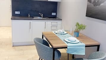Een moderne keuken met witte kasten, een magnetron en een spoelbak. Er staat een eettafel met stoelen en een blauwe tafelkleed. Op de tafel staat een potplant.