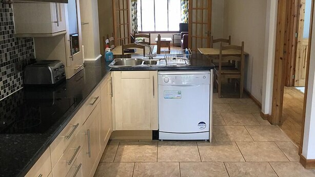 Una cocina compacta con lavavajillas, tostadora y pileta. Se ve un comedor con mesa y sillas a través de una ventana.
