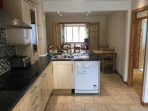 A compact kitchen with a dishwasher, a toaster, and a sink. There is a dining area with a table and chairs visible through a window. - 4 Bedroom House Stratherrick (Inverness)