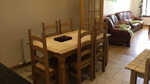 Un comedor con una mesa y sillas de madera, un sofá de cuero marrón y una puerta con paneles de vidrio.