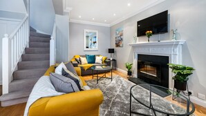Un salon moderne doté d’un escalier, d’une cheminée, d’un téléviseur à écran plat et d’un canapé avec des coussins.