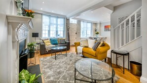 Un salon spacieux avec une cheminée, un canapé, un fauteuil jaune et une table basse en verre.