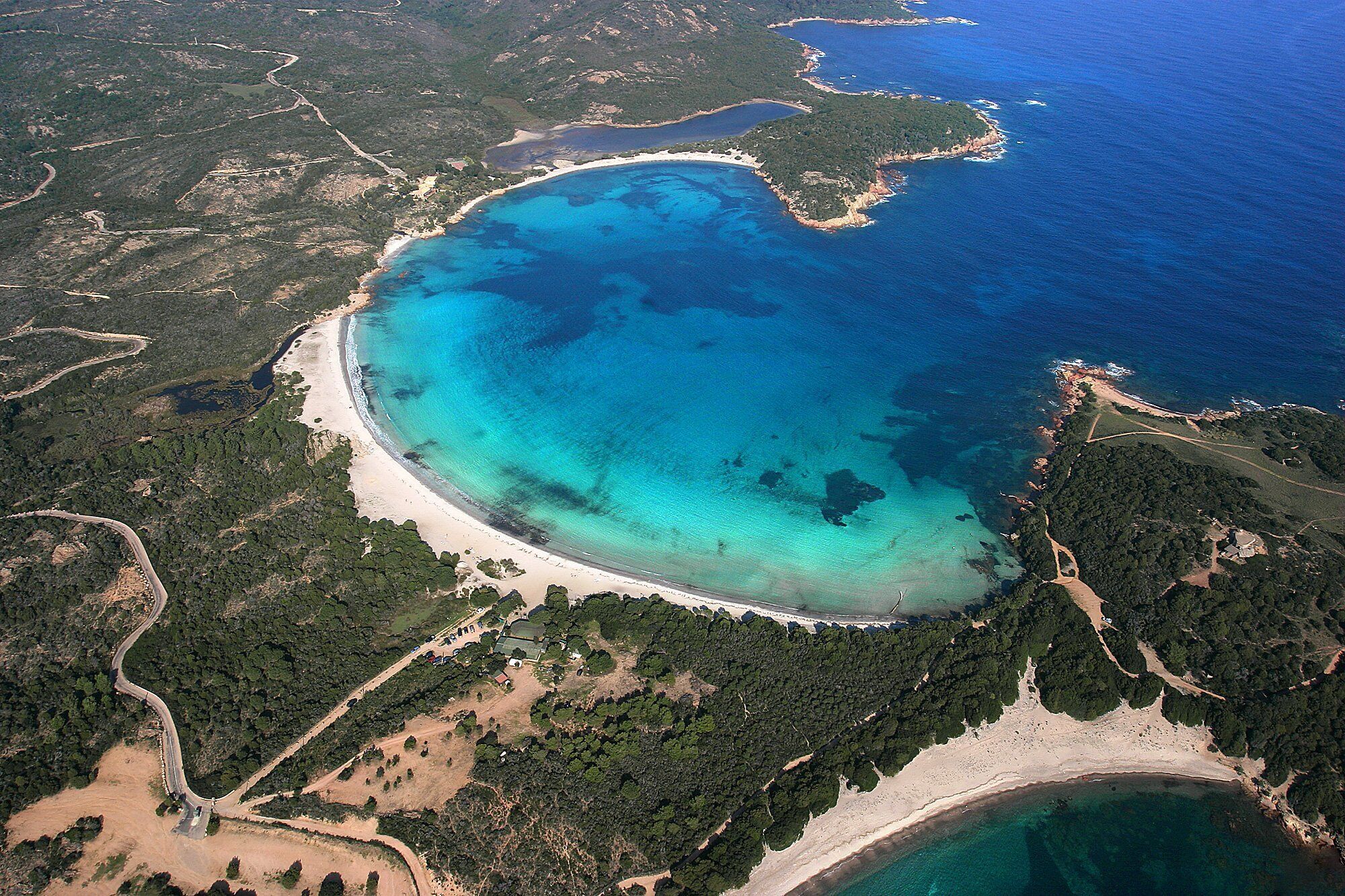 Vista aérea de una zona costera con una gran bahía, playas de arena y densas áreas boscosas.