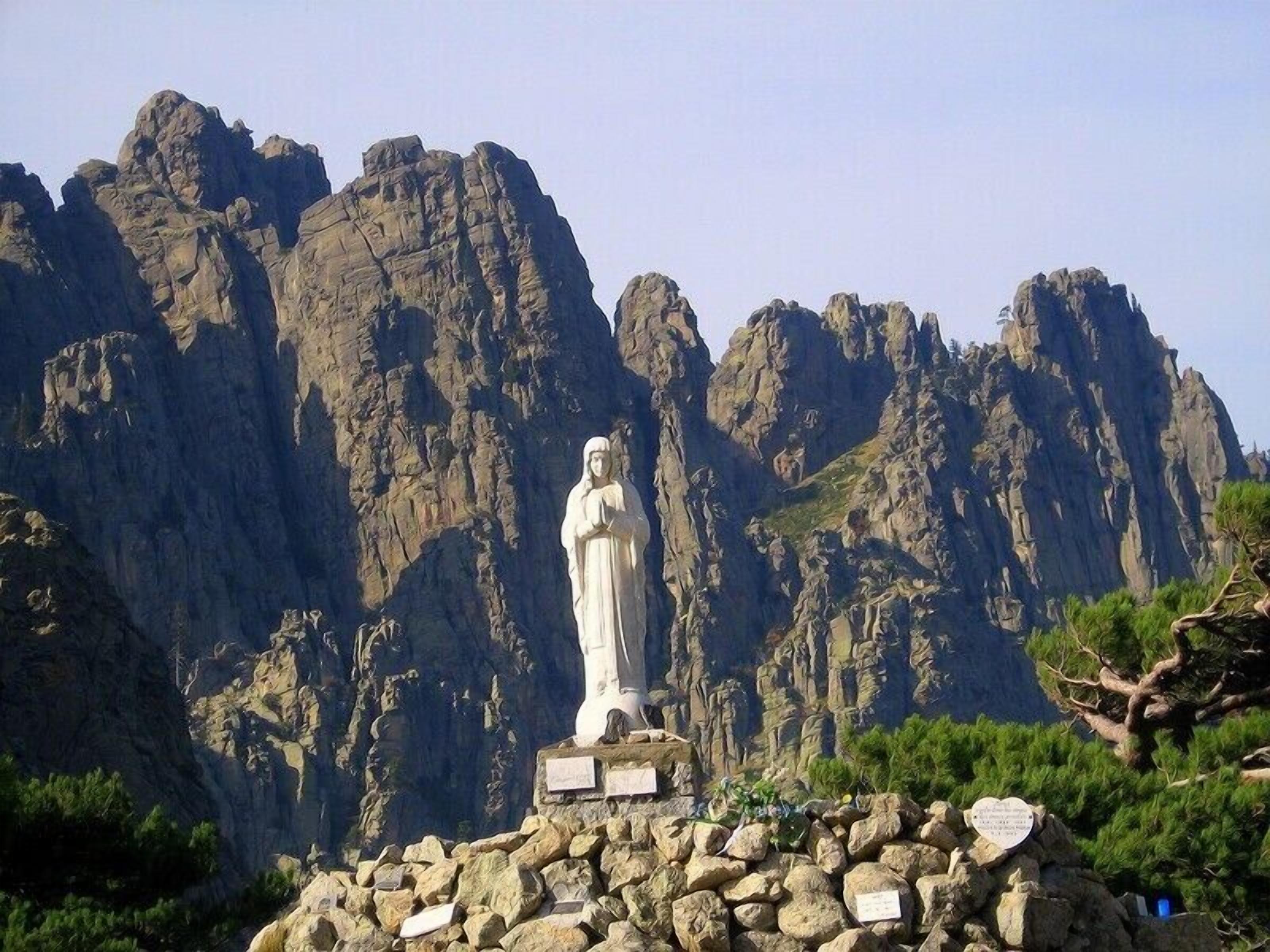 A white statue on a rocky base with a mountainous backdrop.