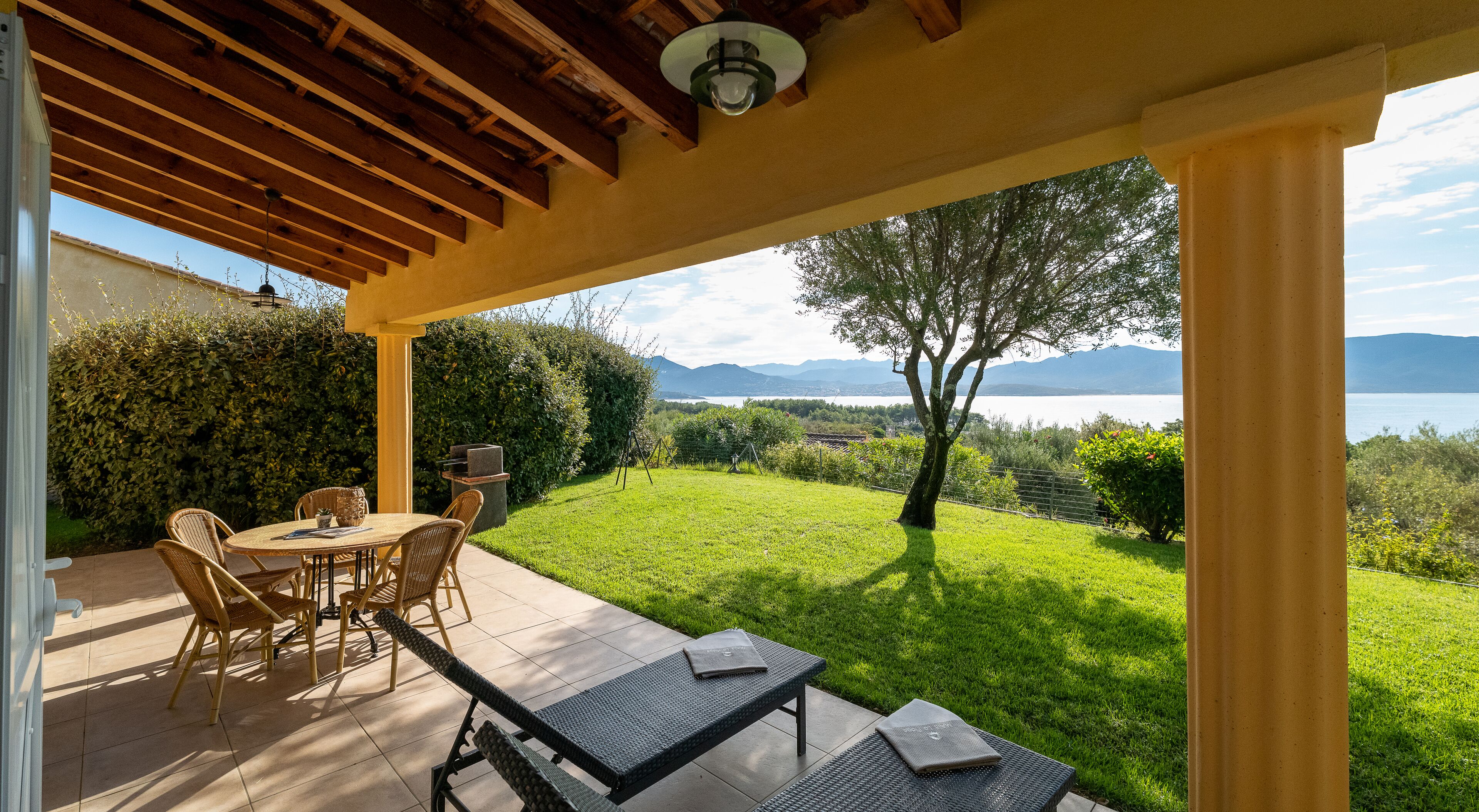 A covered patio with a table and chairs, a grill, and a view of a lake and mountains.