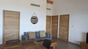 A modern living room with a wooden dining table, a sofa with cushions, and a hanging mirror.