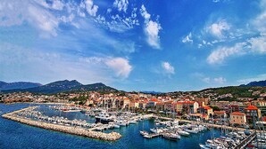 A coastal town with a marina filled with boats, surrounded by colorful buildings and mountains in the background. - Résidence La Plage (Olmeto)