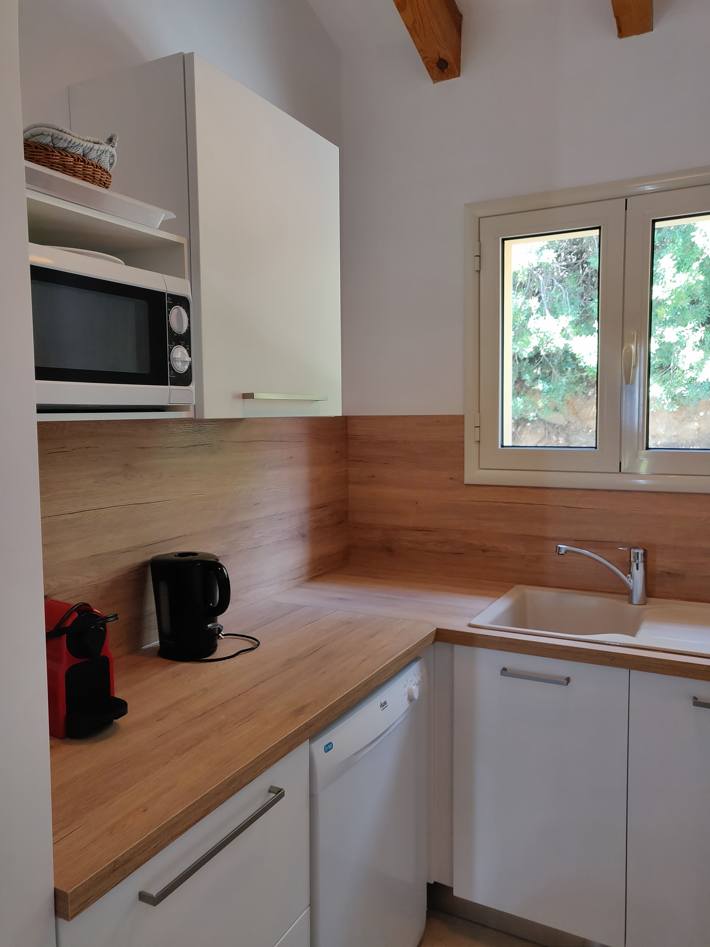 A compact kitchen with white cabinets, a wooden countertop, a built-in microwave, a coffee maker, and a dishwasher.