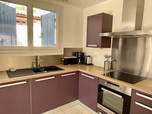 A compact kitchen with a built-in oven, a stainless steel range hood, and a window with a view of the outside.