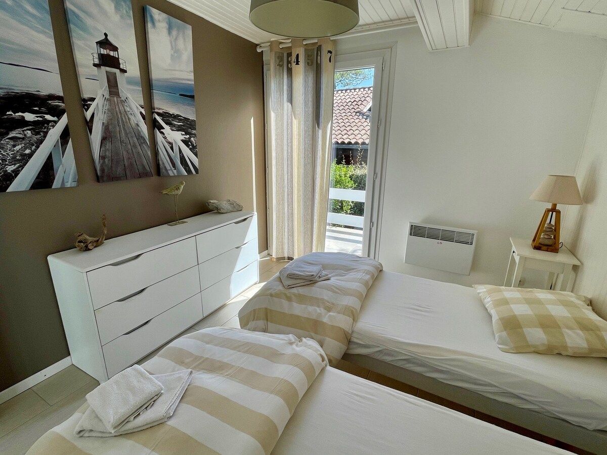 A bedroom with two beds, a white dresser, a nightstand, a lamp, and a painting of a lighthouse.