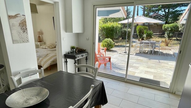 A dining area with a table and chairs, a sliding glass door leading to an outdoor patio with a table and chairs, and a bed visible in the adjacent room. - Perfect holiday home in Hourtin-Plage with wifi and very close to the beach (Hourtin)