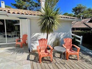A patio with three Adirondack chairs, a round table, and a palm tree.