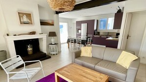 A modern living room with a sofa, a wooden coffee table, a purple rug, a white chair, a fireplace, and a kitchen in the background. - Perfect holiday home in Hourtin-Plage with wifi and very close to the beach (Hourtin)