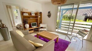 A living room with a sofa, coffee table, TV, and a balcony with a view. - Perfect holiday home in Hourtin-Plage with wifi and very close to the beach (Hourtin)