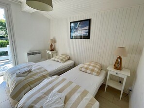 Et hotelværelse med to senge, et vindue, et vægmonteret fjernsyn og et natbord med en lampe.