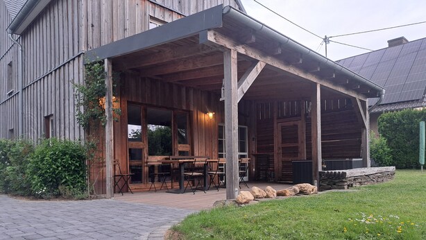 Un edificio de madera con un porche cubierto y mobiliario exterior.