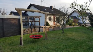 Un columpio de madera con asiento rojo en un jardín cubierto de césped.