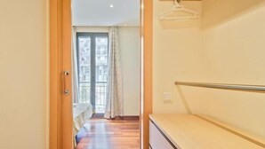 A hallway leading to a bedroom with a wooden floor, a bed with a white duvet, and a window with curtains. - Alcam Anglesola (Barcelona)