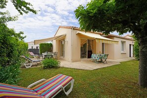 Une maison dotée d’un patio, d’un espace extérieur couvert aménagé en salon et d’une pelouse.