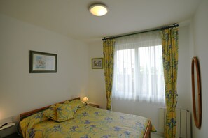 A bedroom with a bed, a bedside lamp, a framed picture on the wall, and a window with curtains. - Charming Villa (3 *) due south, quiet 5km Royan (Charente-Maritime)