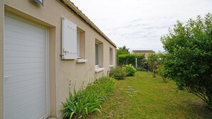 A residential building with a garage door, a small window, and a well-maintained lawn with various plants.
