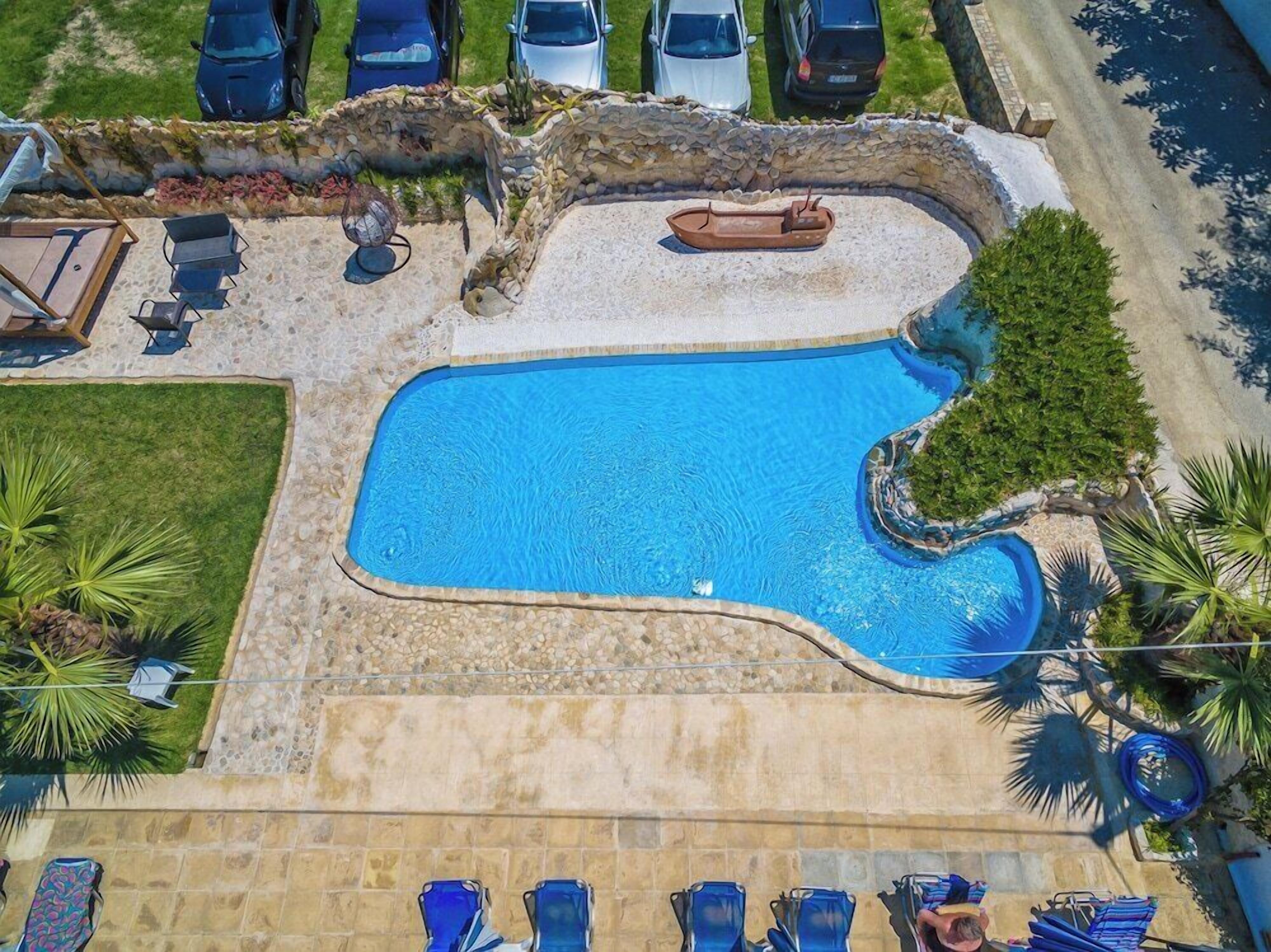 An aerial view of a swimming pool with a stone wall, surrounded by palm trees and a stone deck.