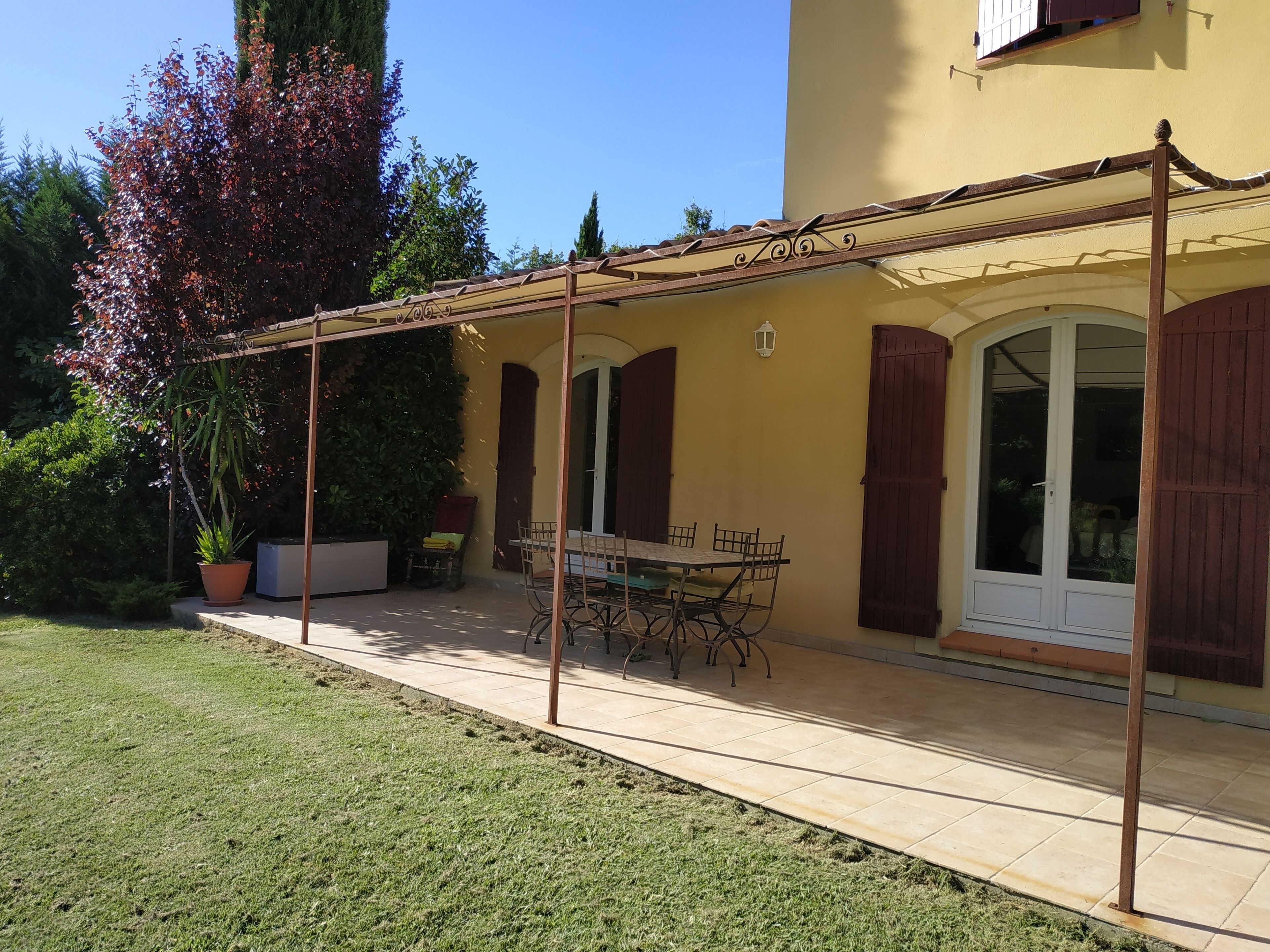 Un patio techado con una mesa y sillas, una planta en maceta y una puerta con ventanal.