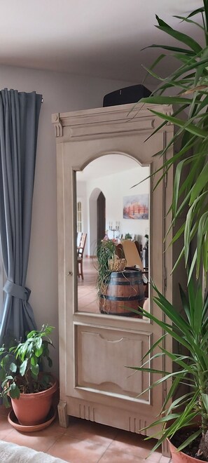 A mirror with a wooden frame, flanked by potted plants, and a view into a room with a dining area. - Magnificent villa for a quiet holiday (Fuveau)