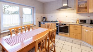 Una cocina moderna con armarios de madera, una mesa de comedor con sillas, un horno empotrado y un ventanal con persianas.