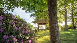 Un cartel en un jardín con arbustos de rododendro y árboles.