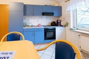 Una cocina con armarios azules, estufa, fregadero y ventana con vista a árboles desnudados.