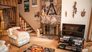 A cozy living room with a fireplace, a television, and a staircase leading to another level. - 126 Ridgepoint 3 Bedroom Townhouse by RedAwning (Avon)