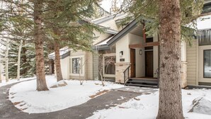 A snow-covered pathway leading to a house with a stone foundation and a wooden door. - 126 Ridgepoint 3 Bedroom Townhouse by RedAwning (Avon)