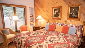 A bedroom with a large bed, a wicker chair, a nightstand with a lamp, and two framed floral paintings on the wall. - 126 Ridgepoint 3 Bedroom Townhouse by RedAwning (Avon)