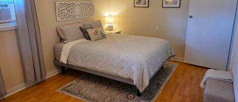 A bedroom with a bed, a nightstand, a lamp, a door, and a window with curtains.
