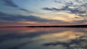 Uno specchio d'acqua calmo con il riflesso del tramonto, cieli sereni e una costa lontana.