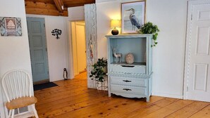 Una stanza con pavimento in legno, una sedia bianca, una cassettiera bianca con soprammobili e una porta con pannello blu.