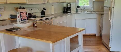 Een keuken met witte kasten, een houten kookeiland met krukken, een magnetron en een koelkast.