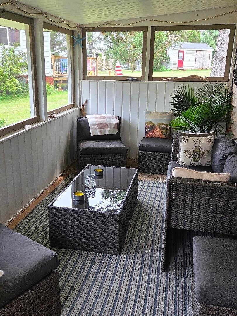 A covered outdoor seating area with wicker furniture, a glass-top coffee table, and a view of the backyard.