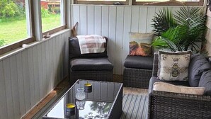 Un espacio de estar al aire libre techado con mobiliario de mimbre, una mesa de centro de vidrio y vista al jardín.