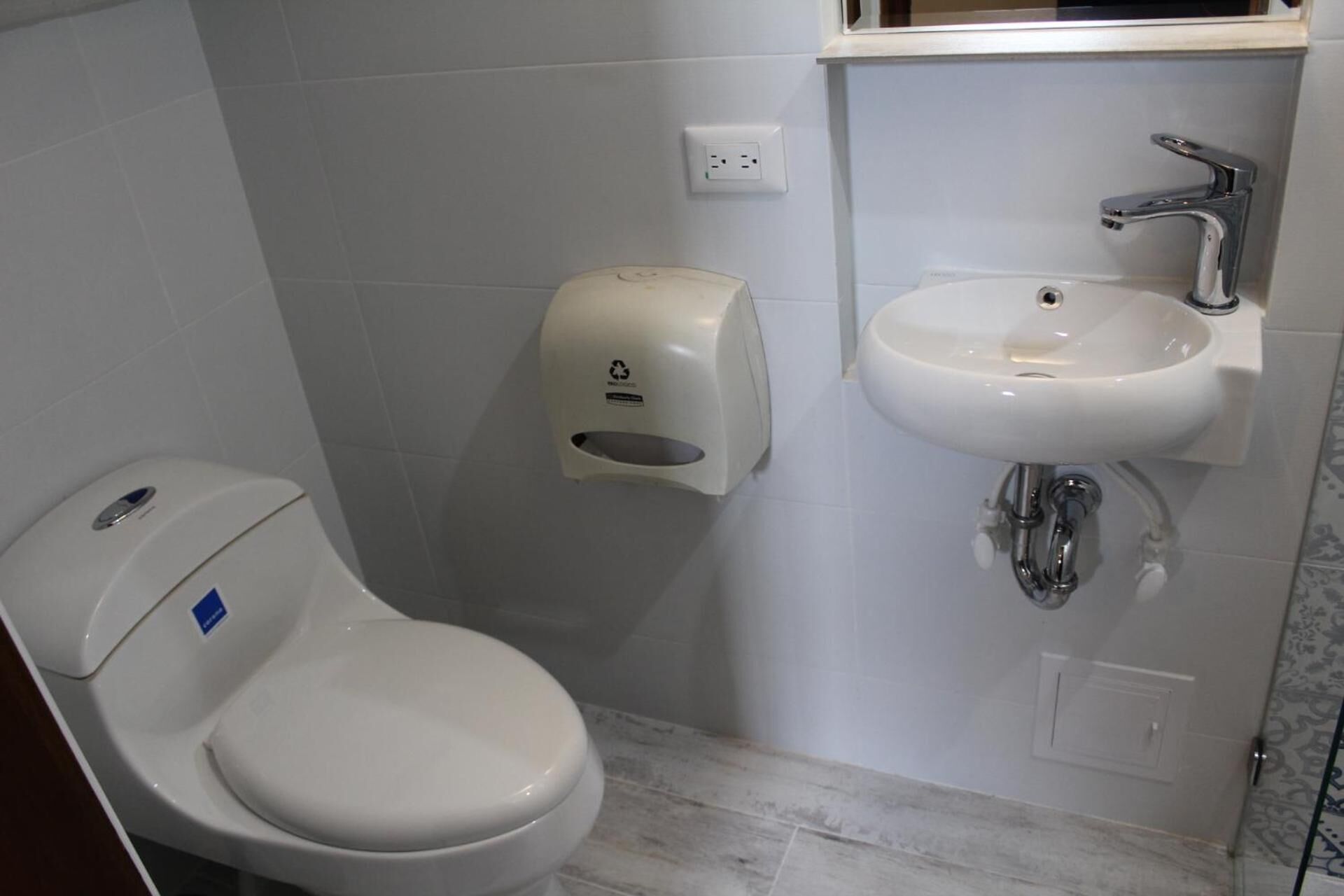 A small bathroom with a toilet, a hand sanitizer dispenser, and a sink.